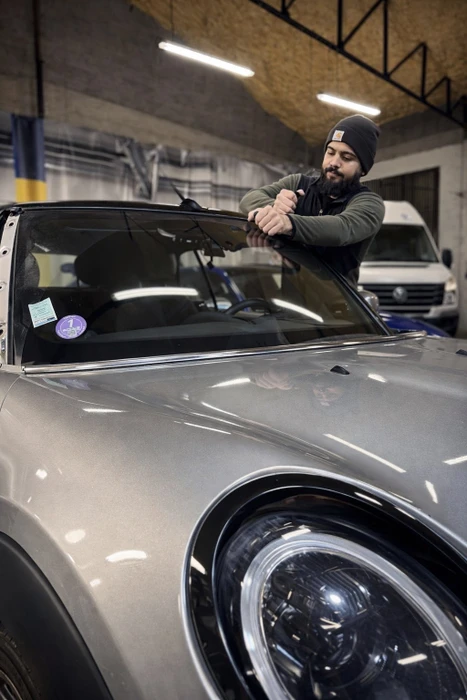 Atelier automobile intérieur avec technicien barbu en bonnet noir travaillant sur vitrage de véhicule gris
