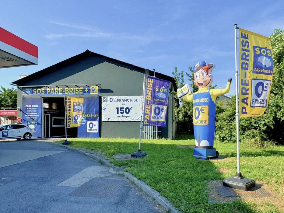Deux techniciens en bleu de travail installent un pare-brise automobile dans un atelier vitrage