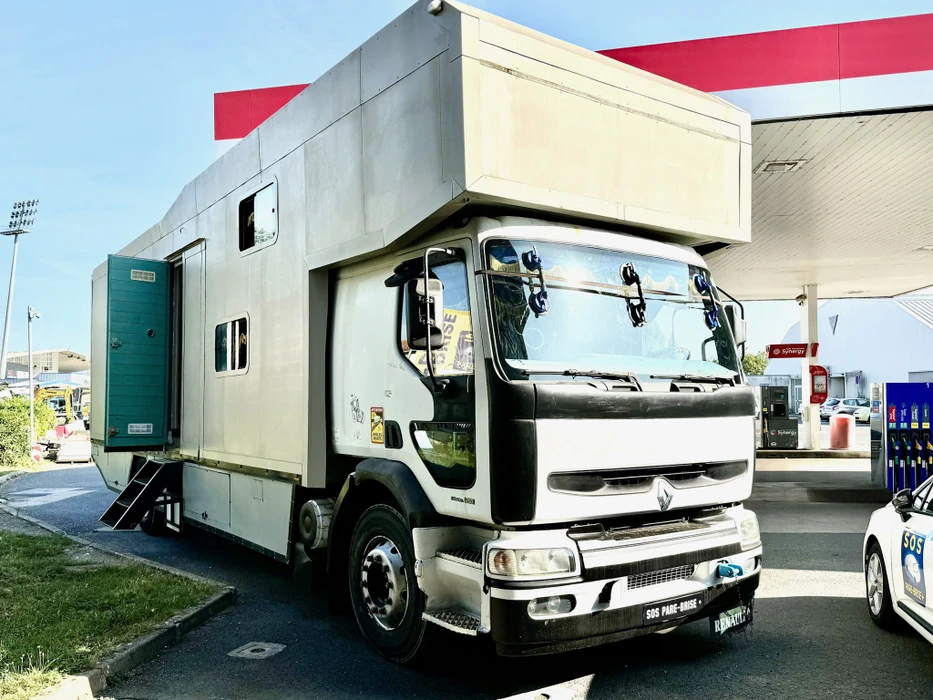 Camion-laboratoire mobile stationné dans une station-service, équipé d'un compartiment arrière surélevé blanc et gris avec fenêtres et porte d'accès latérale verte