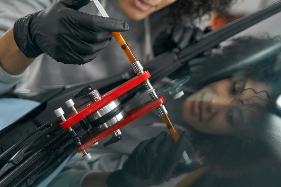 Femme souriante appliquant un film adhésif de protection sur miroir rétroviseur de véhicule dans garage automobile professionnel