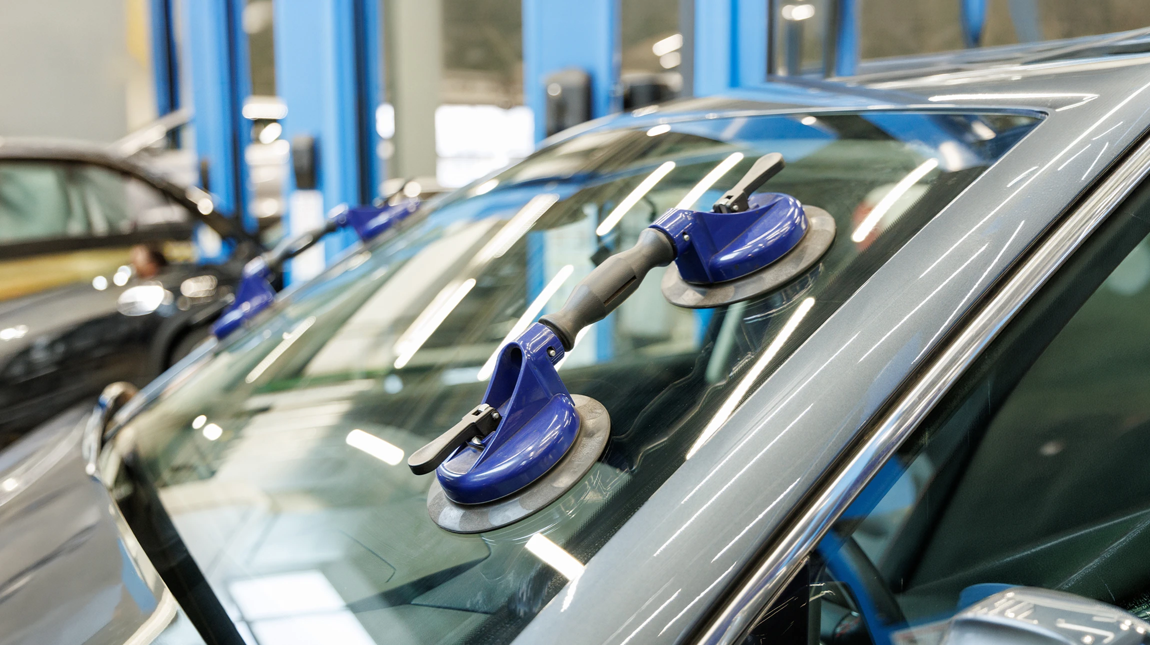 Technicien automobile en combinaison bleue remplace un pare-brise dans un garage