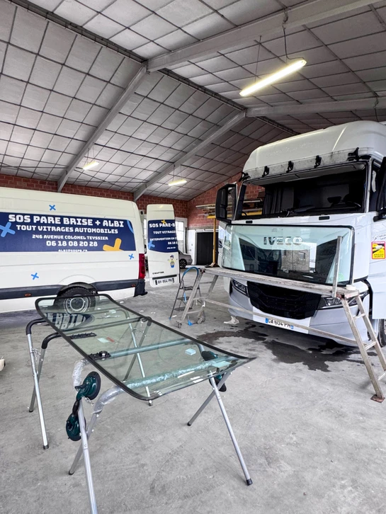 Deux techniciens en bleu de travail installent un pare-brise automobile dans un atelier vitrage